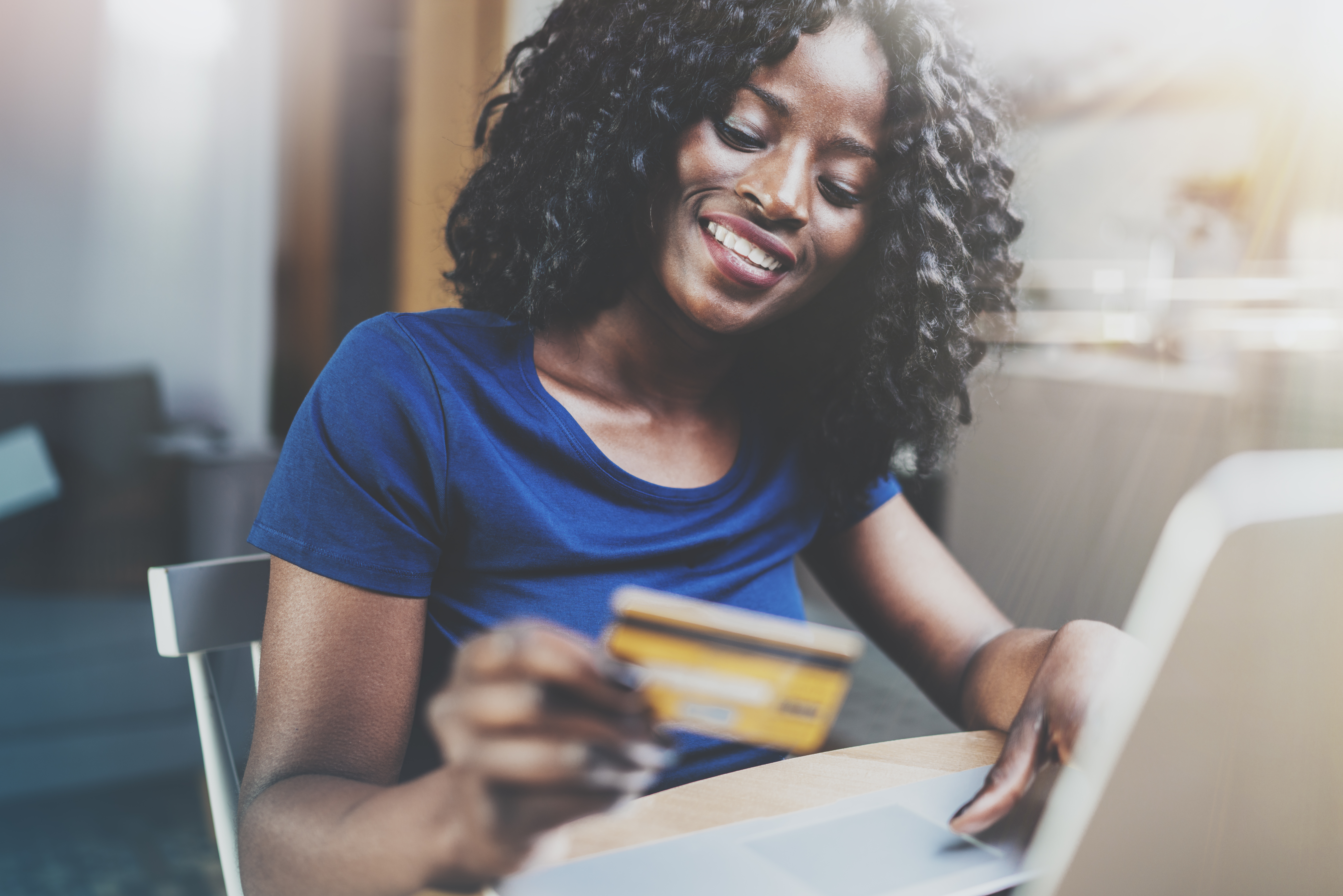A happy African American woman uses her credit card to make an online purchase after learning how to apply for a credit card and get approved.
